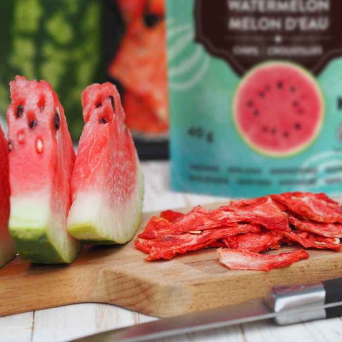 Dried and fresh slices of watermelon on a kitchen board against the background of grates from the dryer with watermelon on a wooden white table. Homemade sweet chips in a dryer.